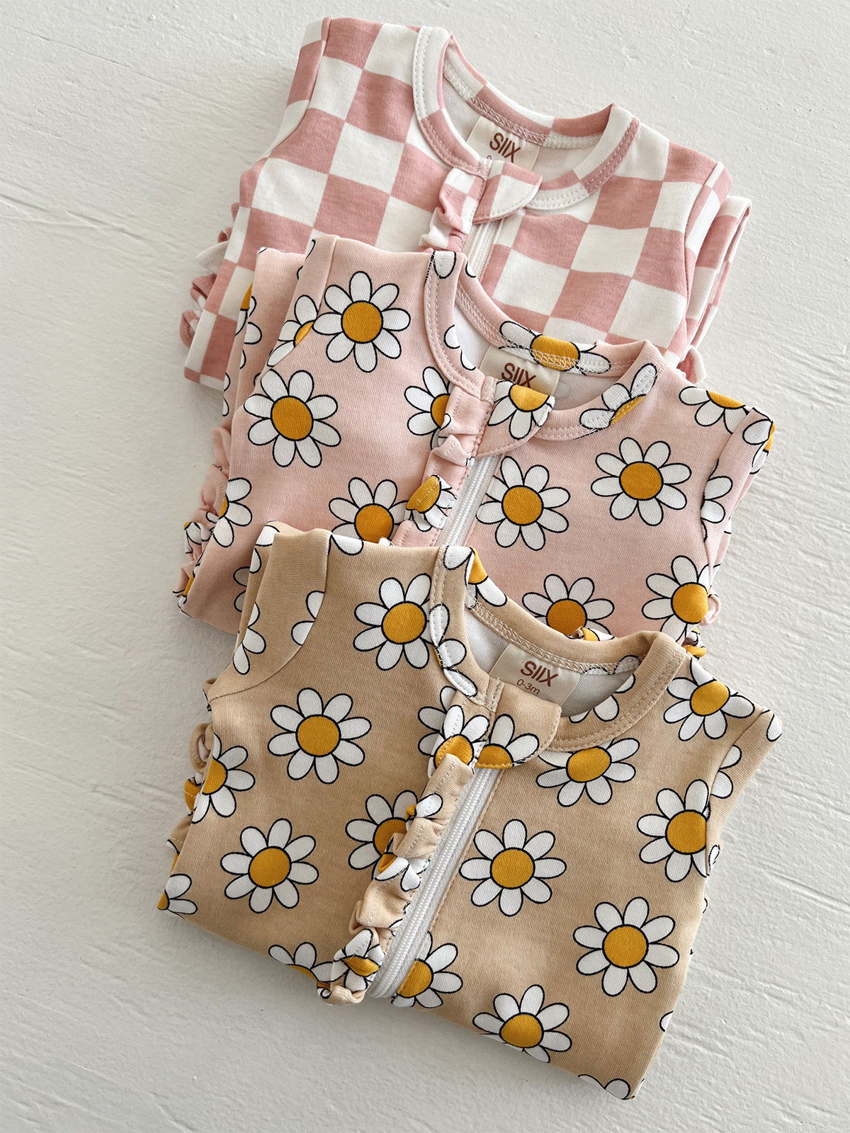 Three baby outfits featuring pink checkered and floral prints stacked on a white surface.