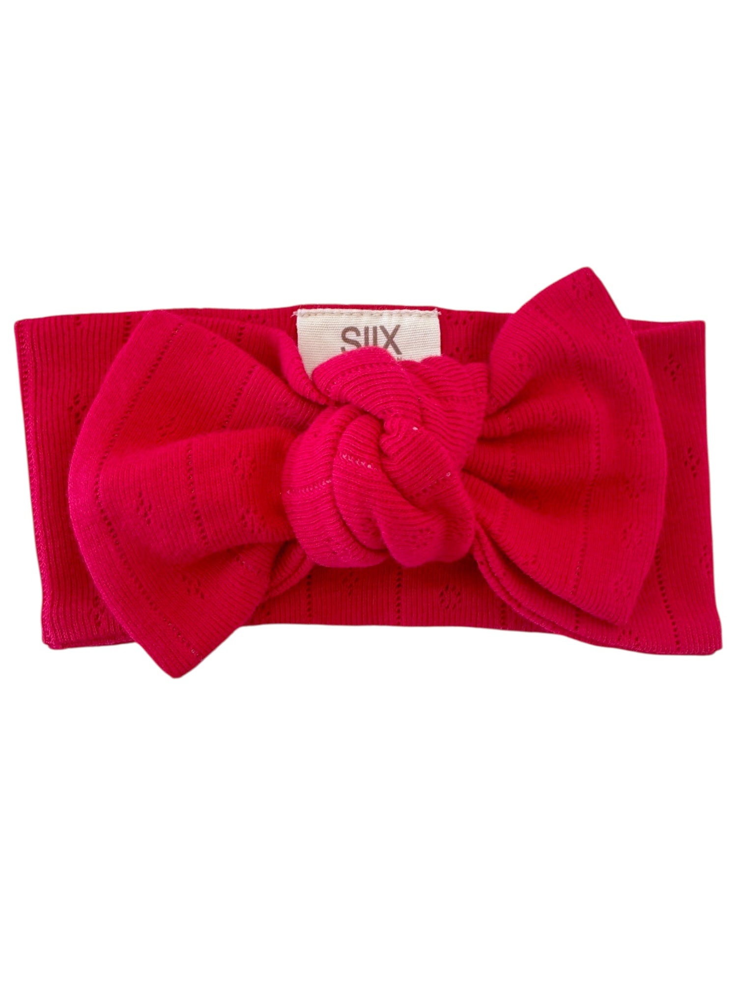 Bright pink headband with a large knot detail, featuring a textured ribbed design and a small tag marked