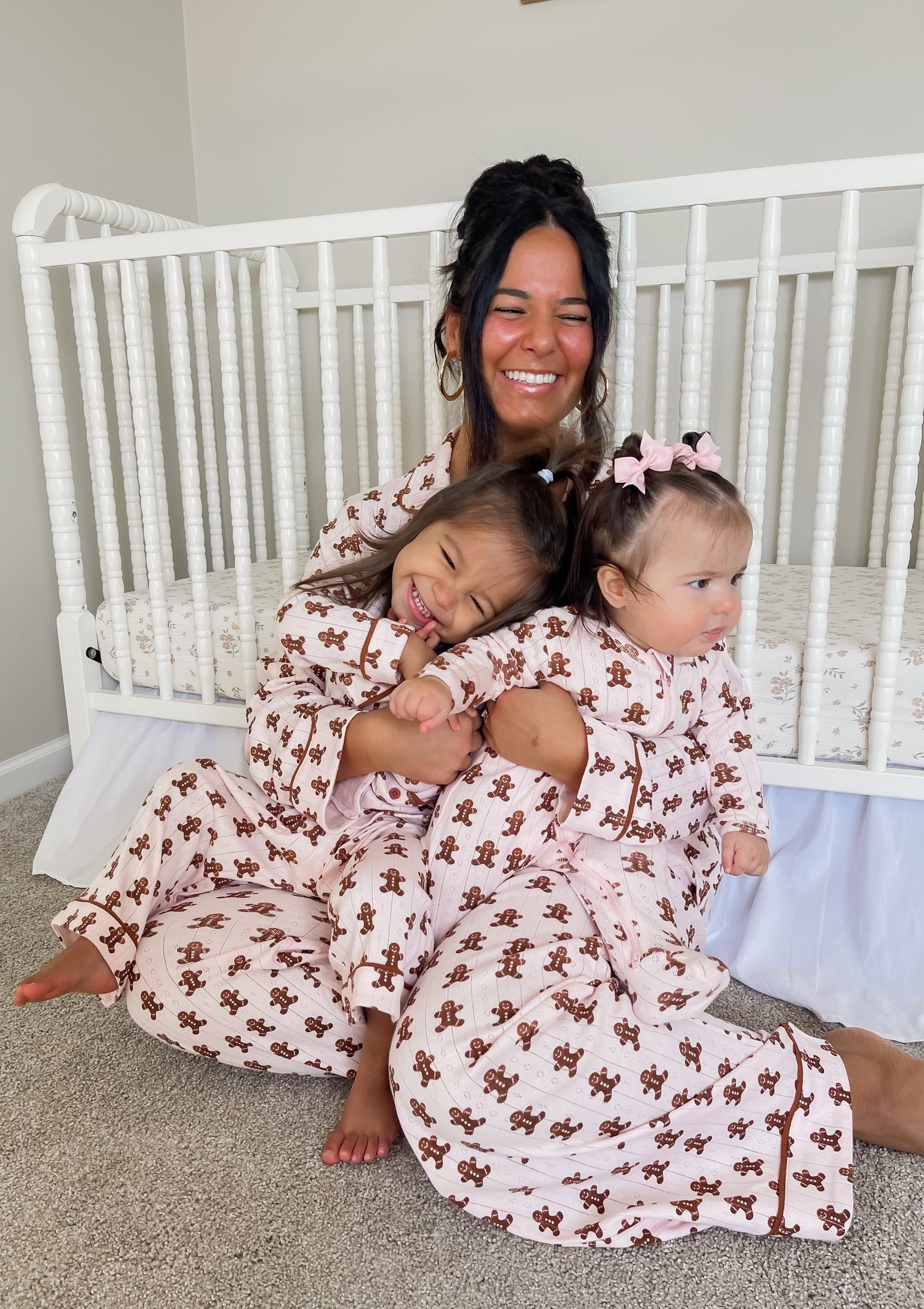 Woman and two girls in matching pajamas smile together in a cozy nursery setting.