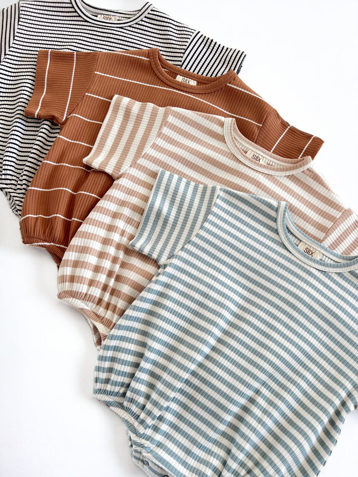 Four striped baby rompers in varying colors: black, rust, beige, and light blue, displayed together on a white background.