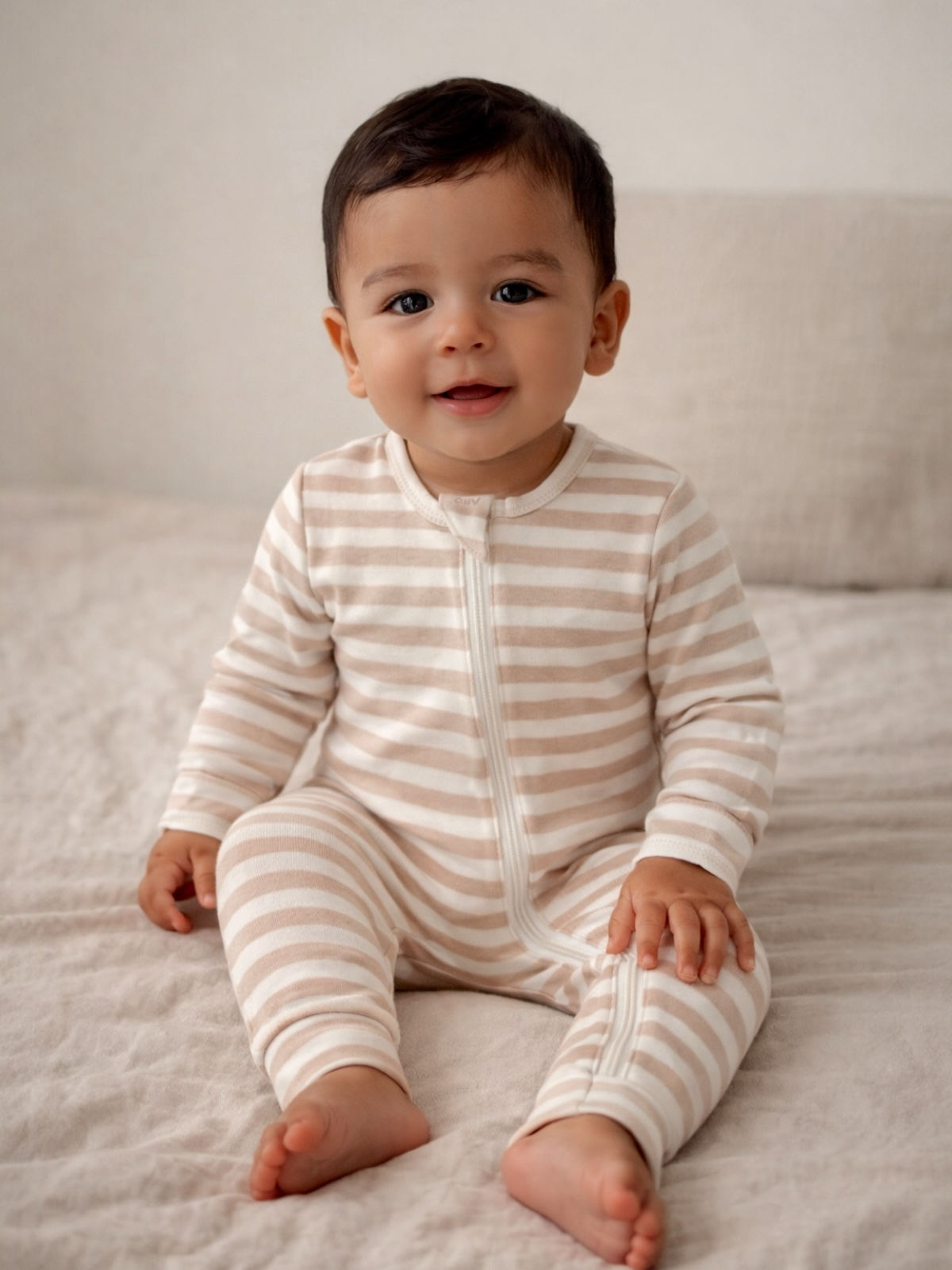 Smiling baby in striped pajama sitting on a soft blanket, showcasing a cozy and cheerful atmosphere.