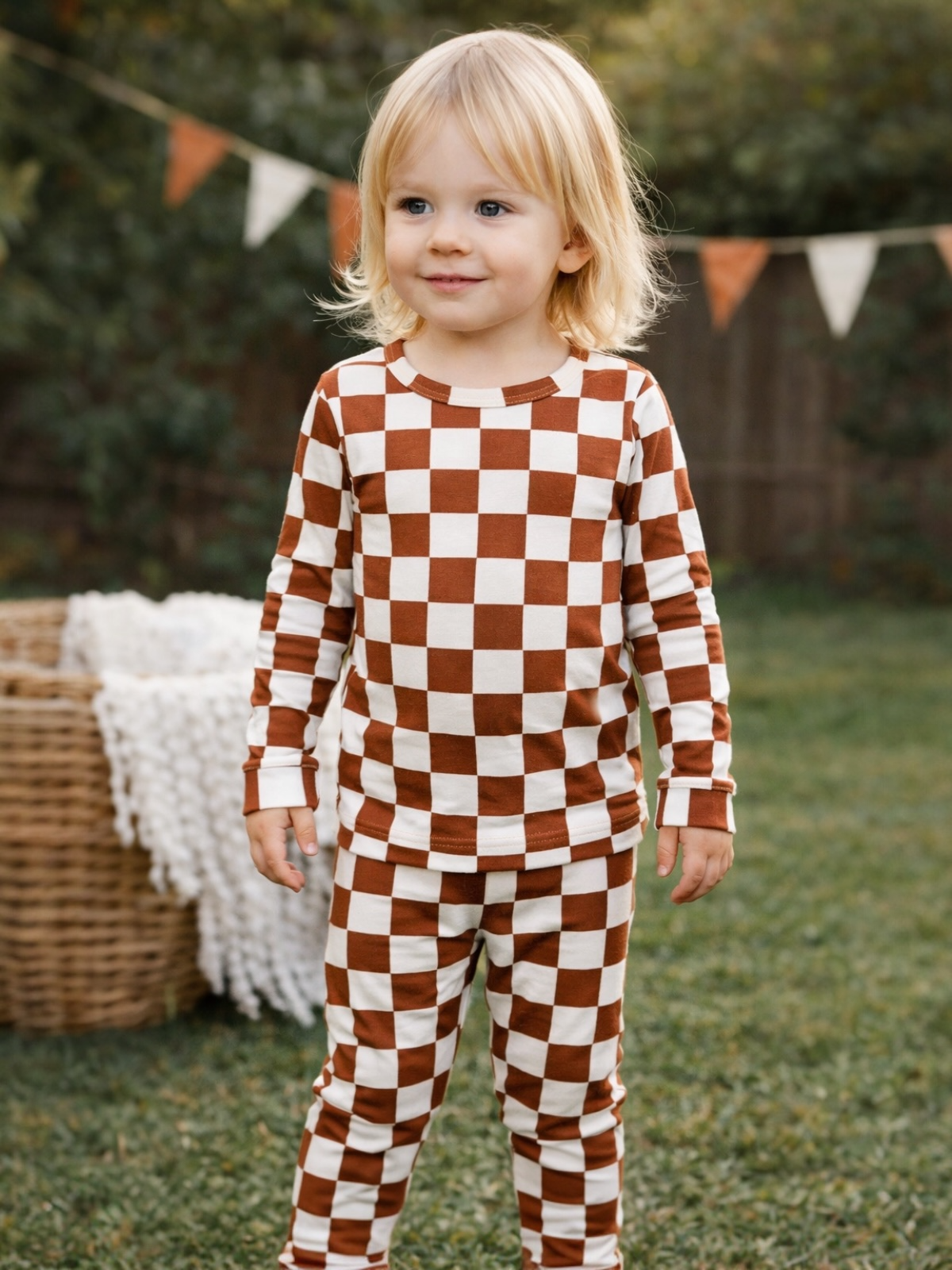 Young child in brown and ivory checkered pajamas, smiling in a grassy outdoor setting.