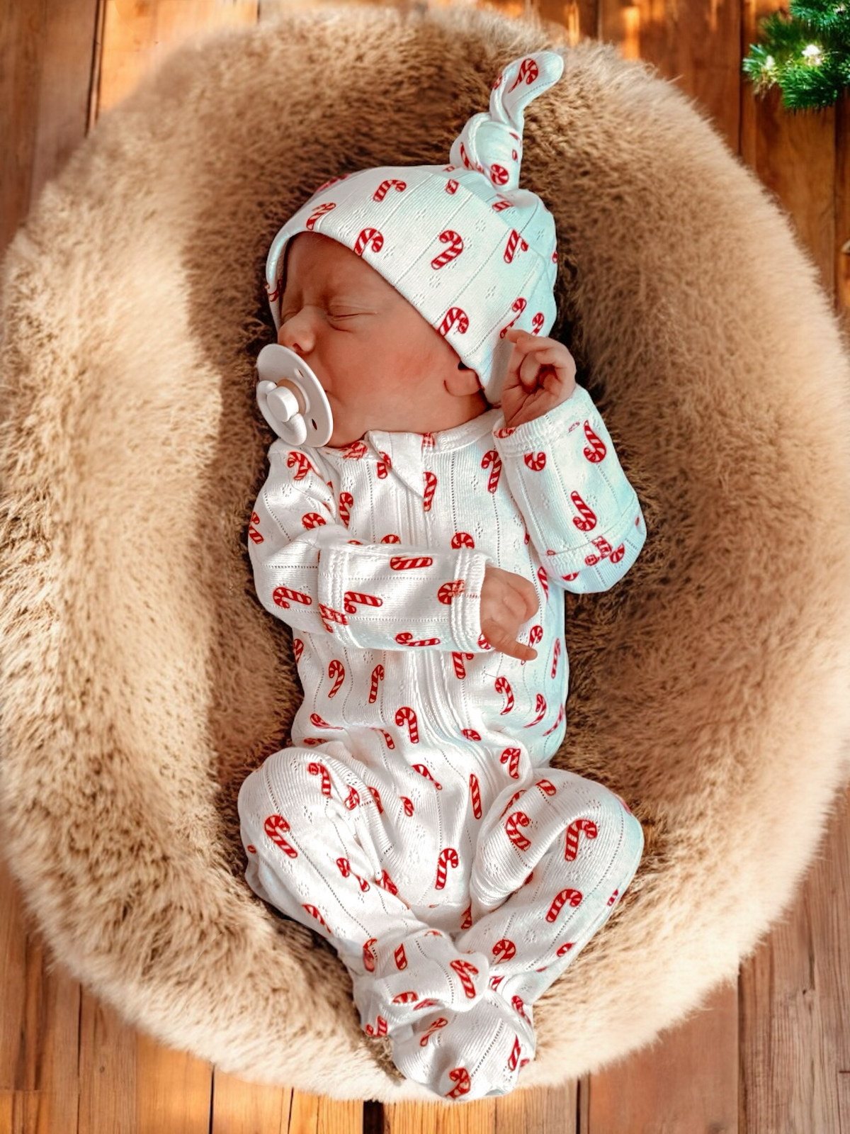 Baby in candy cane-patterned outfit, sleeping peacefully in a cozy, fluffy basket.