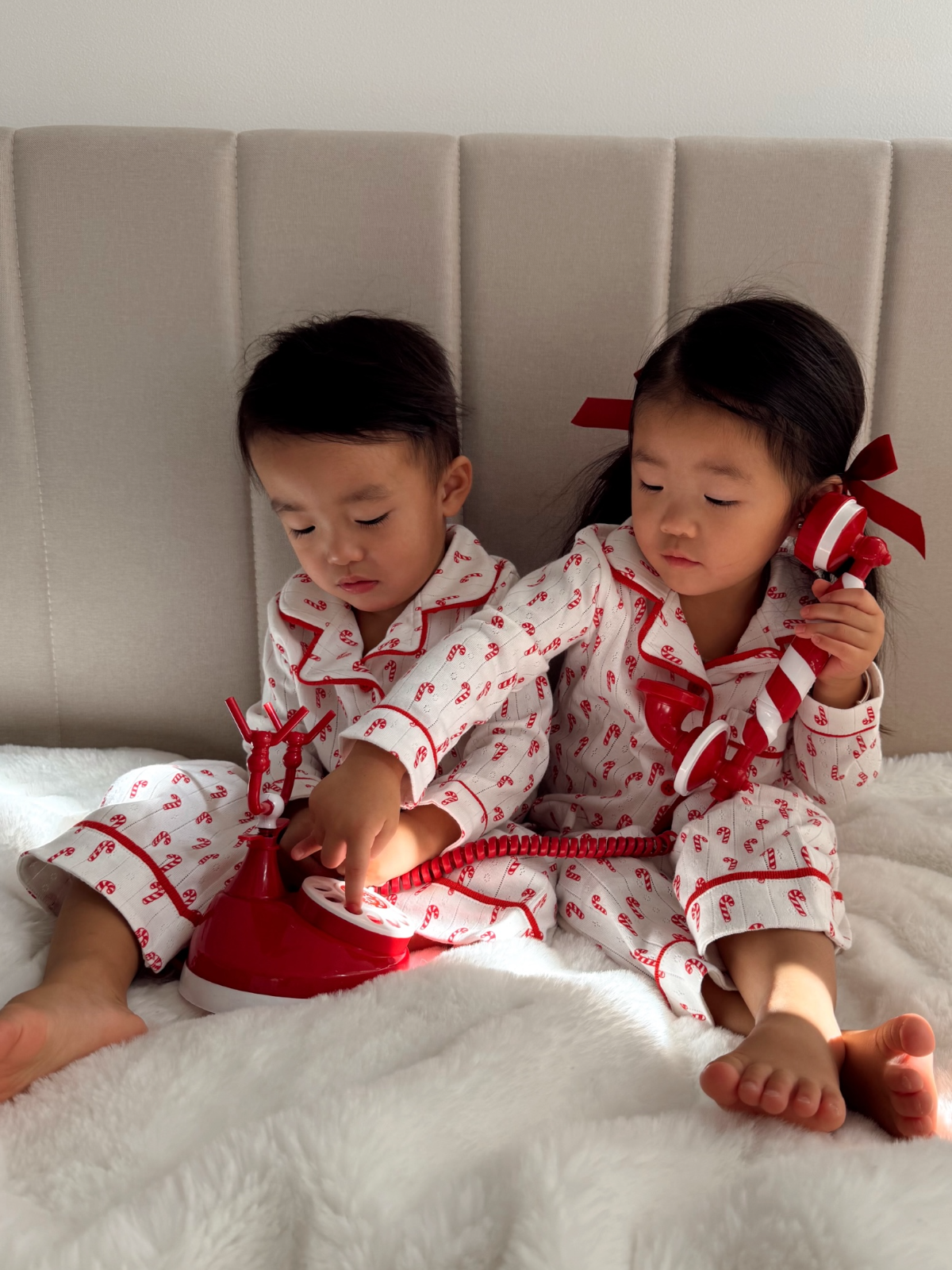Two children in matching red-and-white pajamas playing with a vintage phone on a cozy blanket.