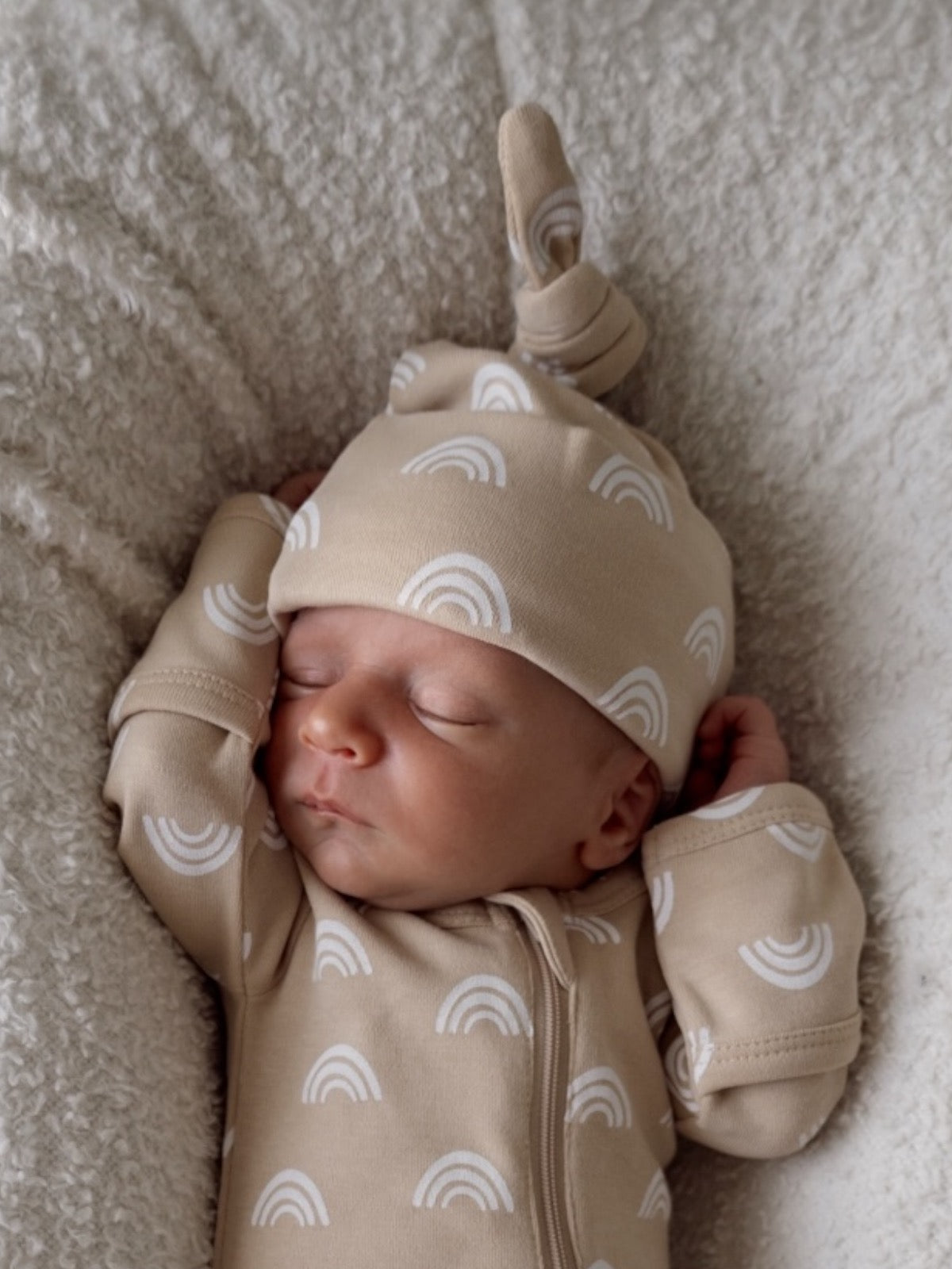 Sleeping newborn in beige rainbow-patterned outfit on a soft blanket.