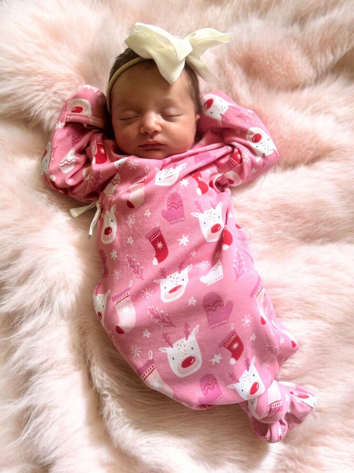 Sleeping newborn in pink patterned swaddle with white bow, resting on a soft, fluffy blanket.