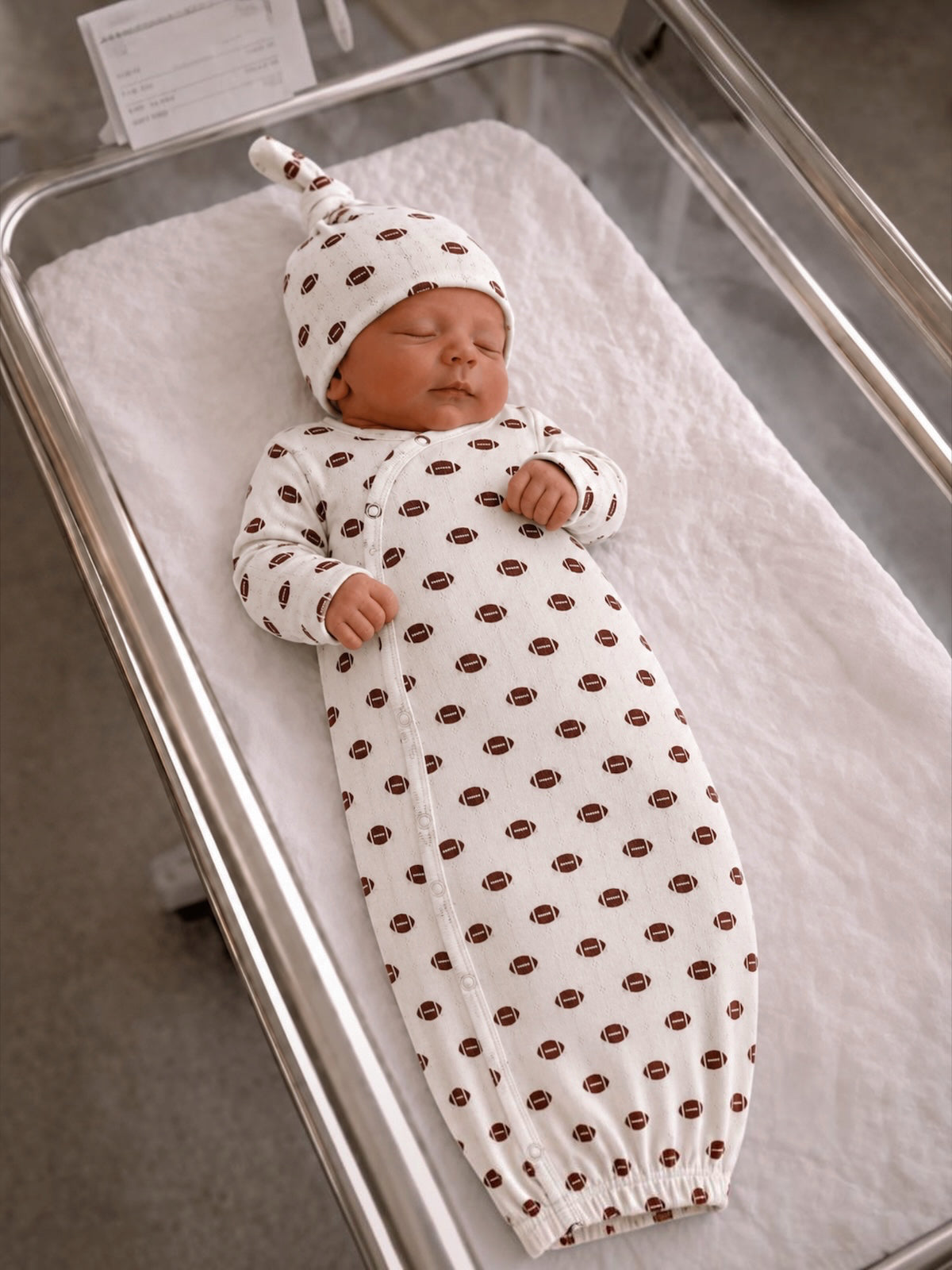Newborn baby in a football-patterned outfit sleeping peacefully in a hospital bassinet.