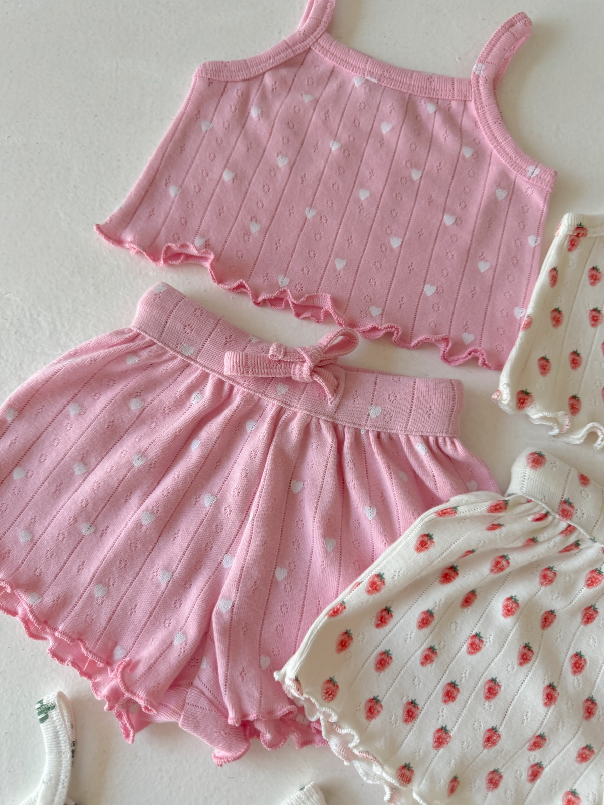 Pink heart-patterned crop top and matching shorts, alongside a white floral-patterned outfit.