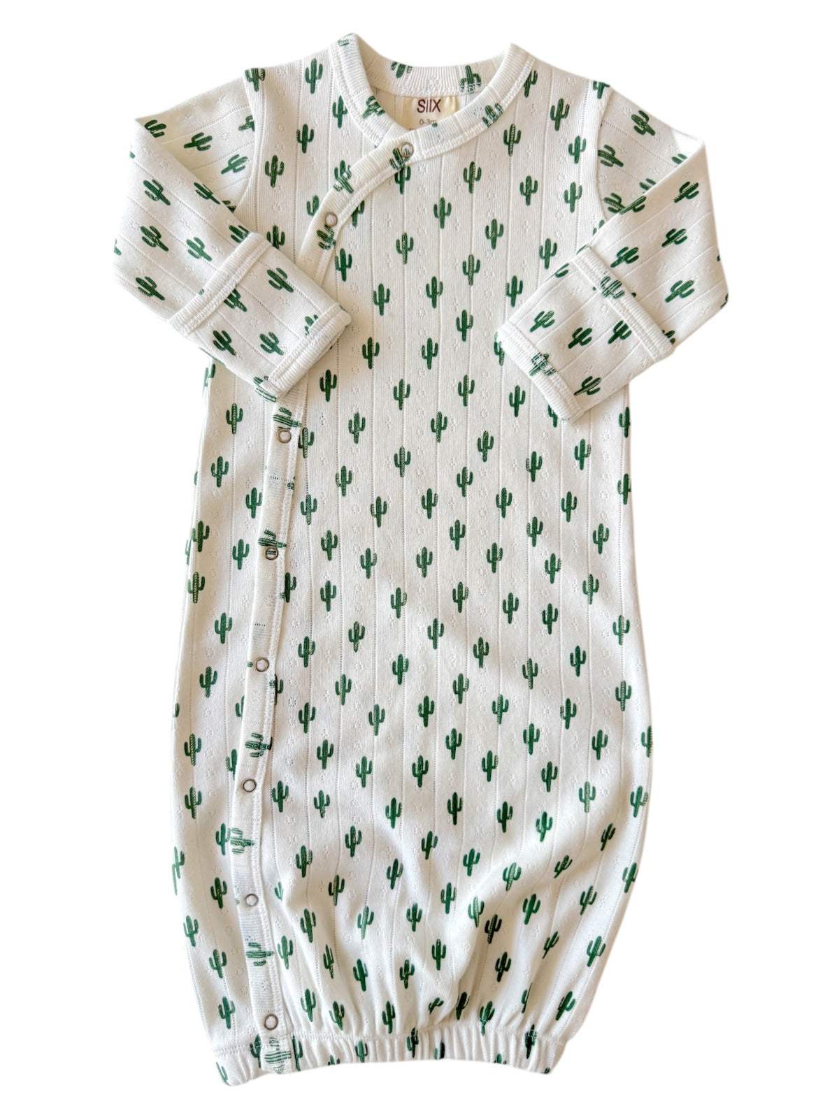 White baby outfit adorned with green cactus prints, featuring snaps along the side and gathered bottom for comfort.