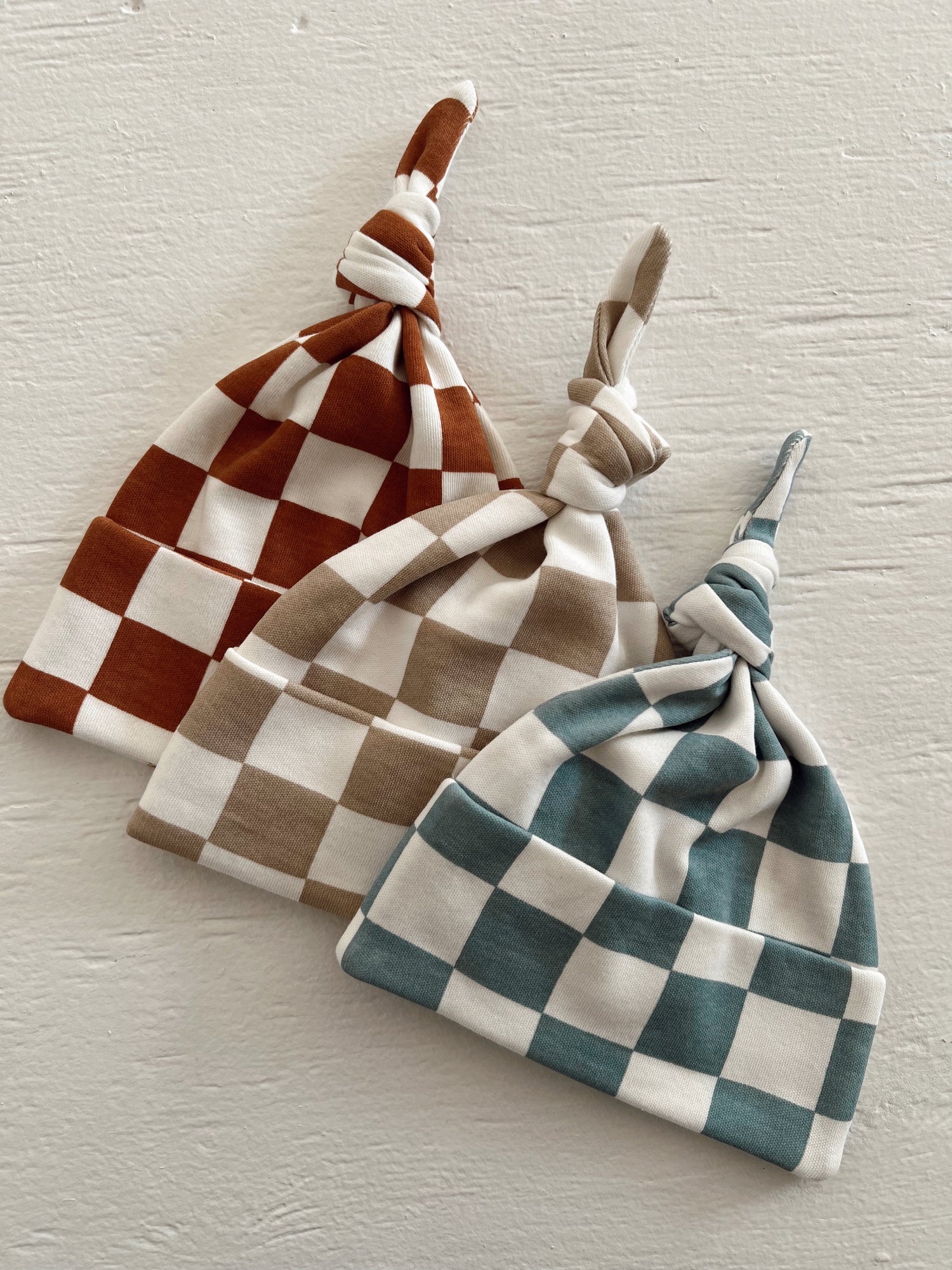 Three checkered hats in orange, beige, and teal, displayed against a textured white background.