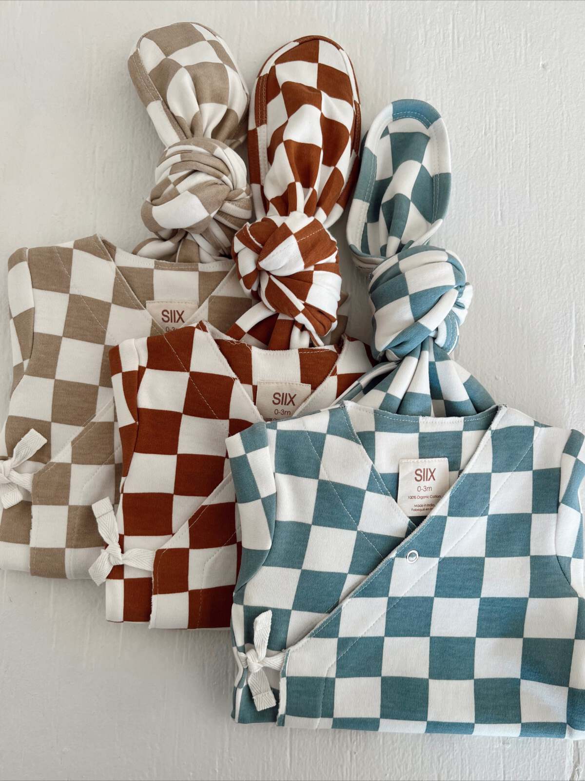 Set of two infant outfits in brown and teal checkered patterns, featuring matching knotted hats.