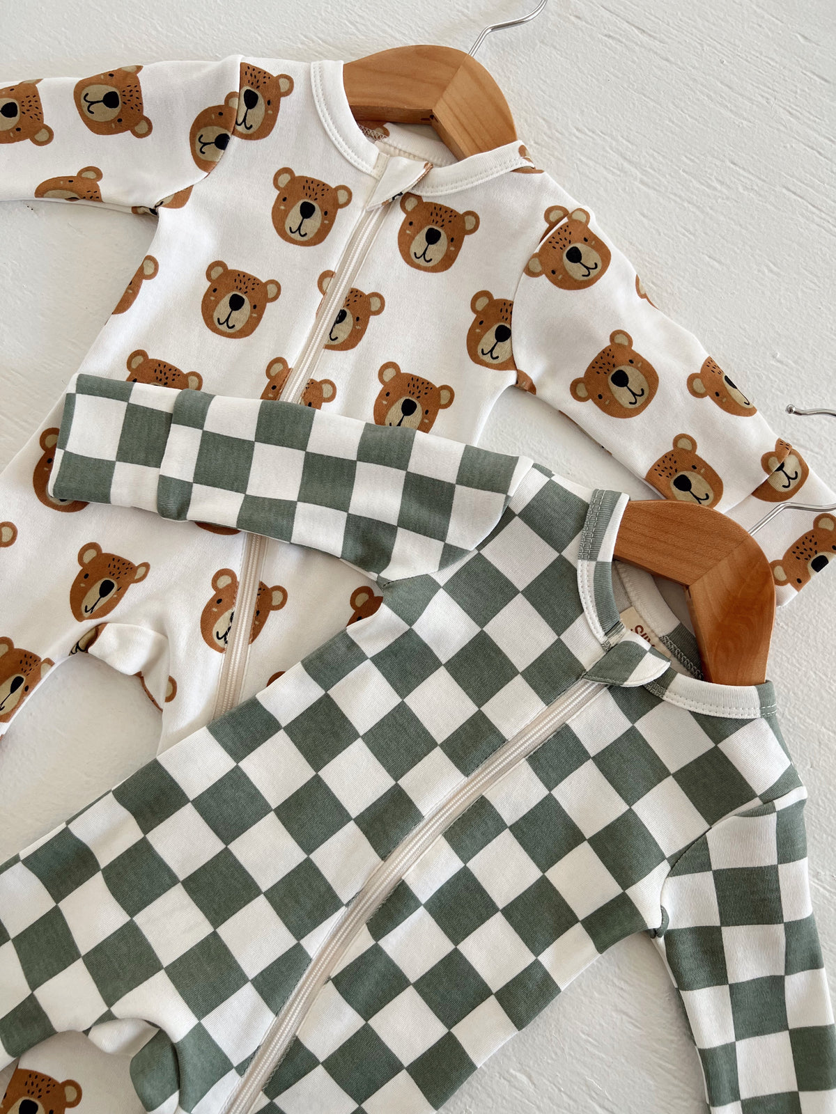 Two children's onesies hanging: one with bear prints, the other in green and white checkered pattern.