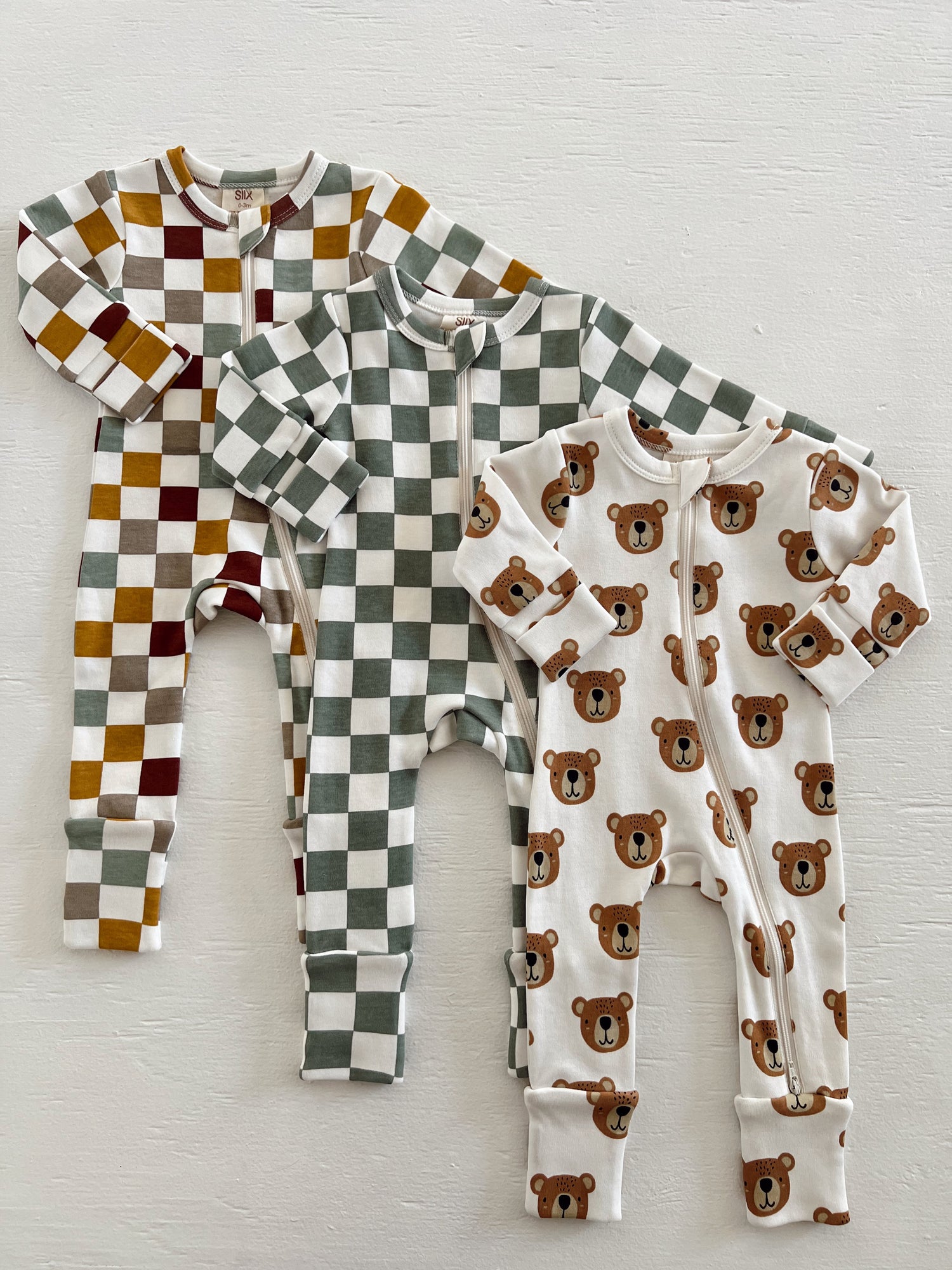 Three baby onesies: two have checkered patterns, and one features a bear print on a white background.