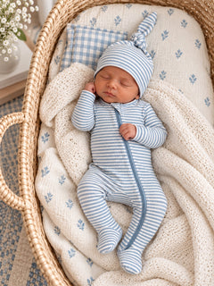 Newborn baby asleep in a cozy bassinet, dressed in blue and white striped sleeper with a matching hat.