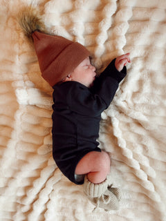 Newborn peacefully sleeping on a plush blanket, wearing a brown beanie and cozy outfit with knit booties.