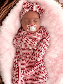 Sleeping baby in heart-patterned outfit with a pink pacifier, nestled on a soft, fluffy pink blanket.