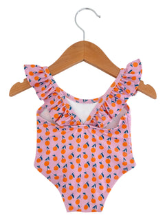Pink swimsuit with orange fruit pattern, featuring ruffled straps, hanging on a wooden hanger.