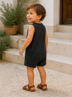 Smiling child in a dark outfit and sandals, standing on outdoor steps surrounded by plants.