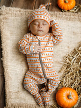 Baby sleeping on a burlap surface, wearing pumpkin-patterned pajamas and hat, with pumpkins nearby.
