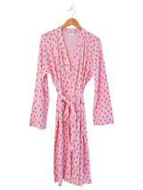 Pink robe with red pattern, long sleeves, and a tie closure, hanging on a wooden hanger.