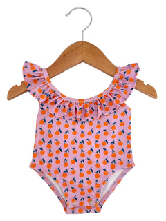 Pink swimsuit with orange cherry print and ruffled neckline, hanging on a wooden hanger against a white background.