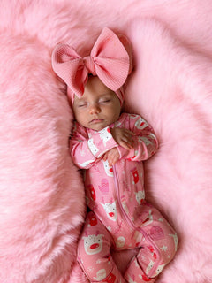 Sleeping baby in pink pajamas with a large pink bow on a fluffy pink blanket.