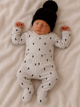 Newborn baby peacefully sleeping in gray outfit with lightning patterns and black hat on a soft blanket.