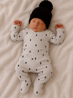 Newborn baby peacefully sleeping in gray outfit with lightning patterns and black hat on a soft blanket.