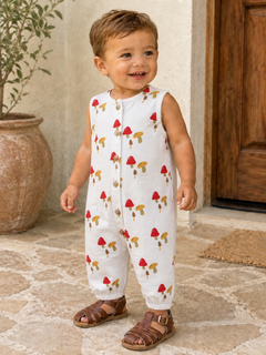 Smiling toddler in a mushroom-patterned outfit, standing on a stone floor near a decorative pot.