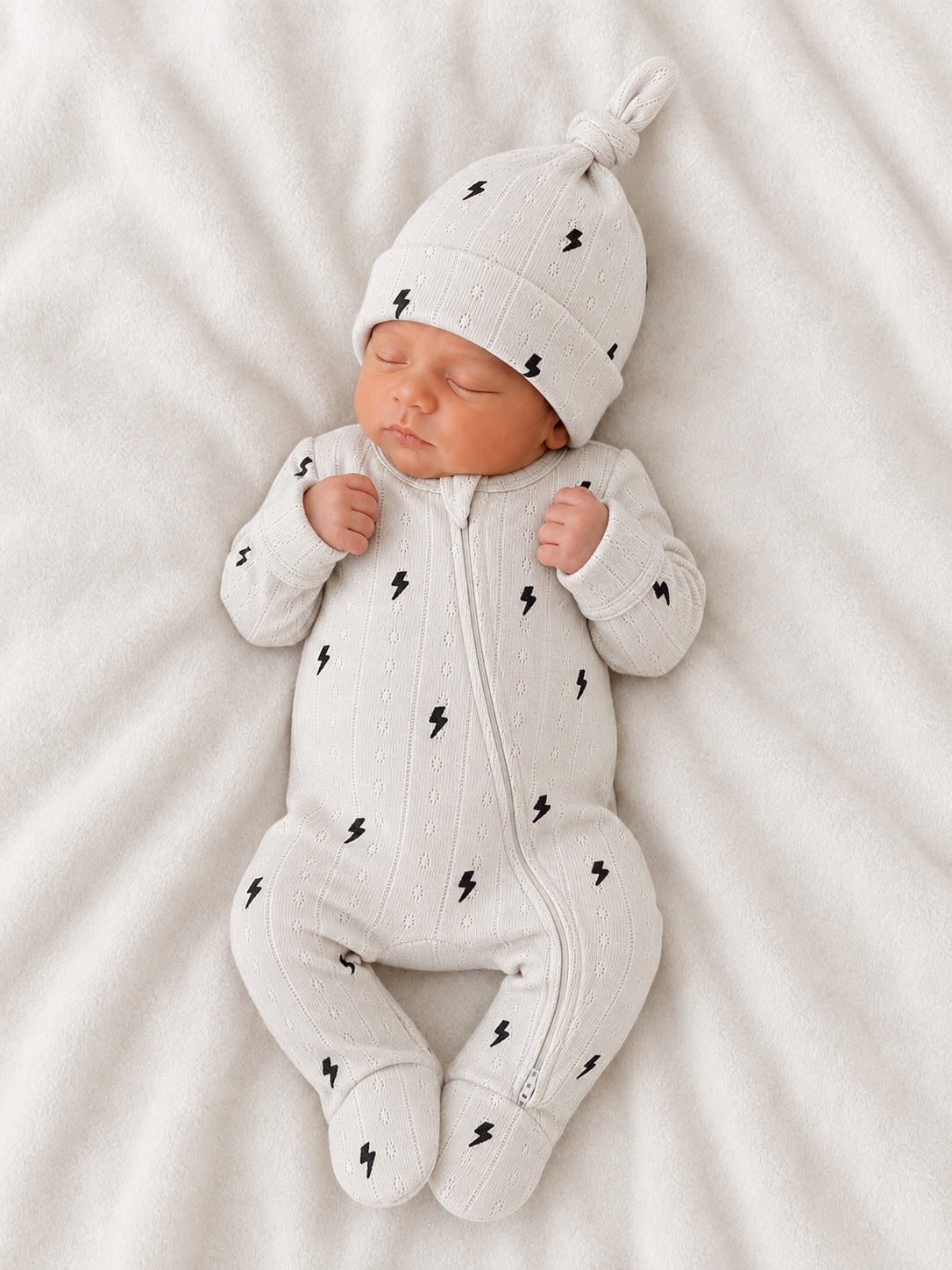 Newborn baby in a light gray outfit with lightning bolt patterns, peacefully sleeping on a soft blanket.