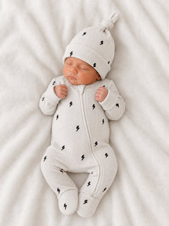 Newborn baby in a light gray outfit with lightning bolt patterns, peacefully sleeping on a soft blanket.
