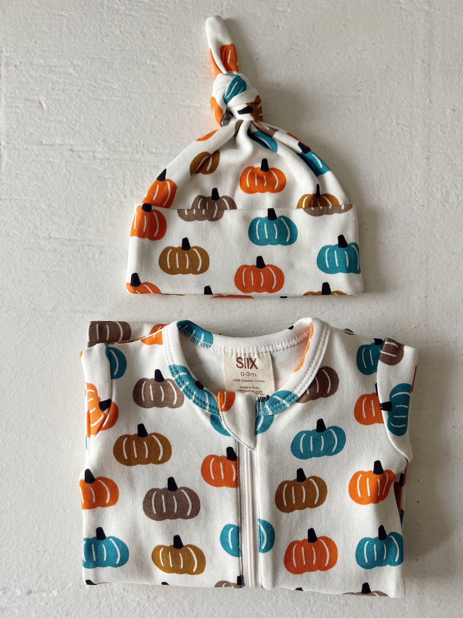 Infant clothing set featuring a pumpkin print onesie and matching knotted hat in autumn colors.