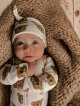 Baby in bear-patterned outfit and hat, lying on a cozy knitted blanket, with big expressive eyes.
