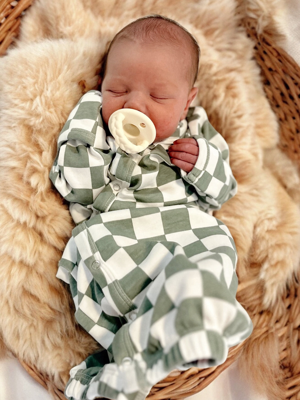 Baby peacefully sleeping in green and white checkered outfit, nestled in a cozy basket on soft faux fur.