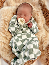 Baby peacefully sleeping in green and white checkered outfit, nestled in a cozy basket on soft faux fur.