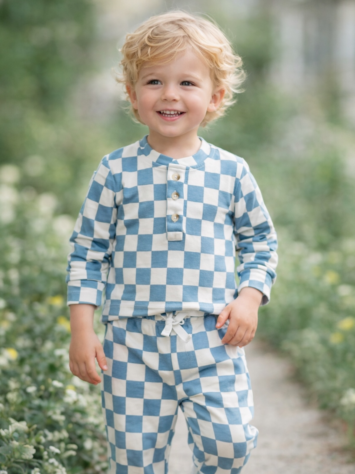 Smiling child wearing blue and white checkered pajamas, walking through a garden path.