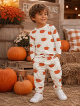 Smiling boy in pumpkin-patterned pajamas by pumpkins, with a cozy autumn backdrop.