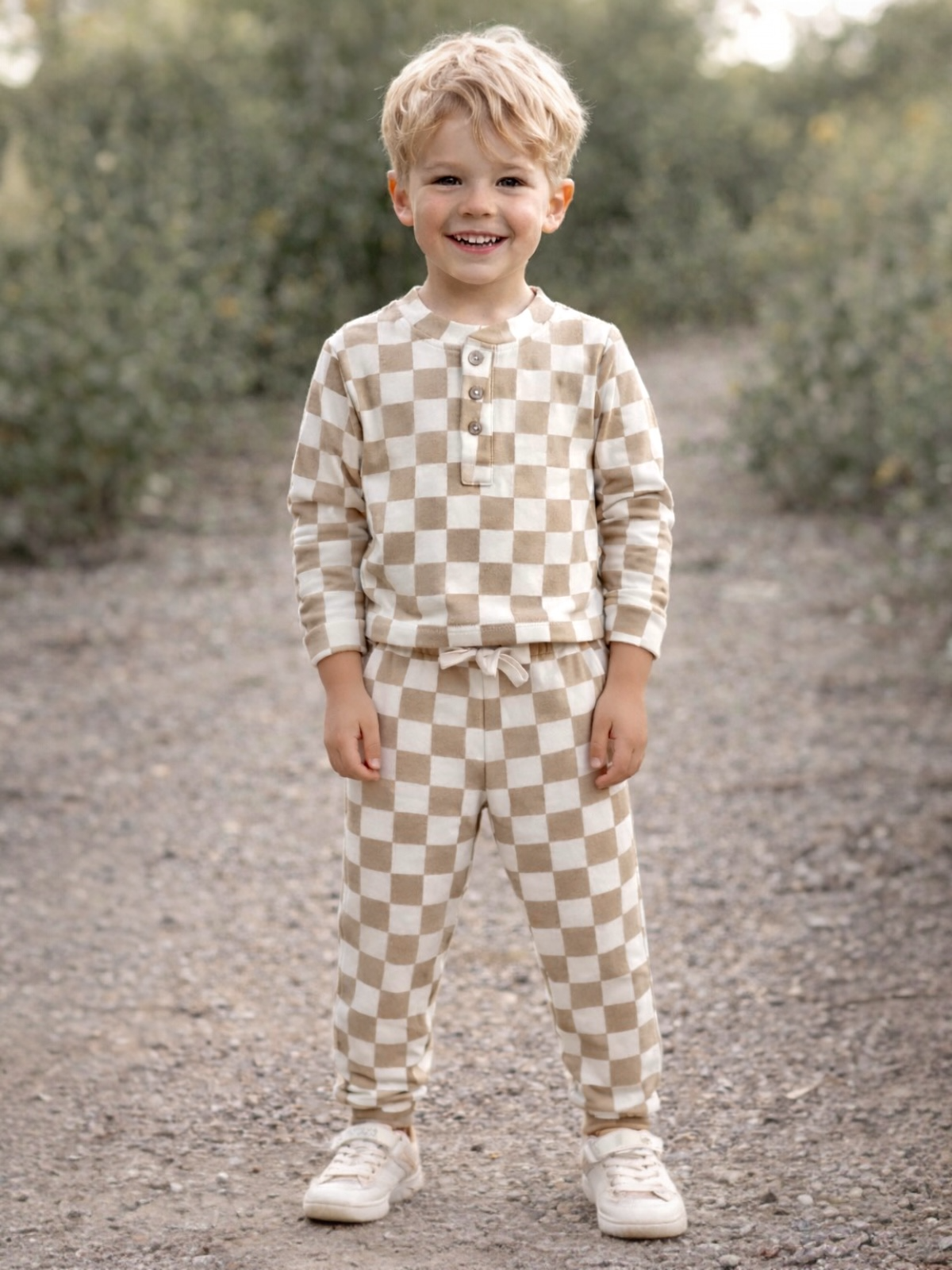 Smiling child wearing brown and cream checkered pajamas, standing outdoors on a gravel path.