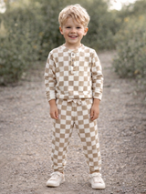 Smiling child wearing brown and cream checkered pajamas, standing outdoors on a gravel path.