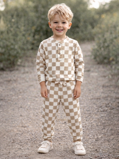 Smiling child wearing brown and cream checkered pajamas, standing outdoors on a gravel path.
