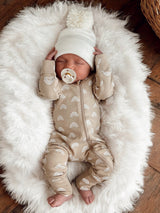 Baby sleeping on a fluffy white blanket, wearing a beige onesie with rainbow patterns and a cozy white hat.