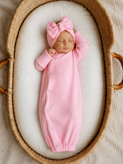 Newborn baby girl in a pink ribbed outfit and bow, peacefully sleeping in a cozy woven basket.