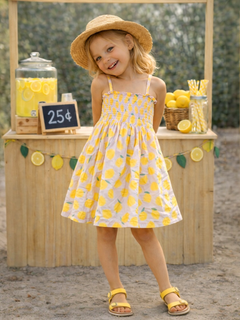Smiling girl in a lemon-patterned dress and straw hat at a lemonade stand, with lemons and a price sign in the background.