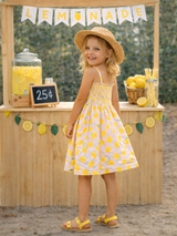 Smiling girl in a lemon print dress stands at a lemonade stand with a yellow lemonade banner and decorations.