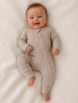 Smiling baby in a beige onesie, lying on a textured white blanket.