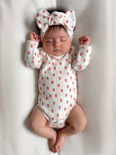 Baby girl sleeping on a soft blanket, wearing a floral onesie and a large bow headband.