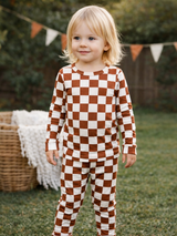 Young child in brown and ivory checkered pajamas, smiling in a grassy outdoor setting.