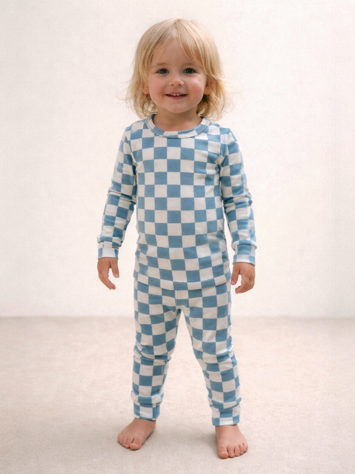 Smiling child in blue and white checkered pajamas standing on a light-colored floor.
