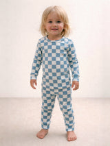 Smiling child in blue and white checkered pajamas standing on a light-colored floor.
