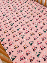 Pink fabric with a repeated pattern of colorful golf carts and small white golf balls. Ideal for playful decor.